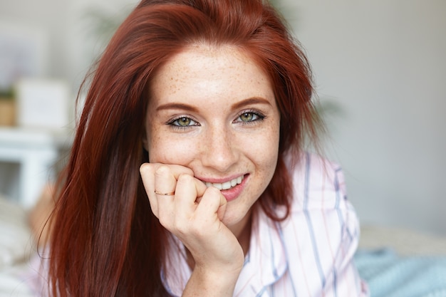 Ciérrese encima del retrato de la mujer caucásica joven pelirroja atractiva con los ojos verdes y la piel pecosa perfecta que pasa la mañana en la cama, en pijama. Belleza, juventud, ocio, gente y estilo de vida