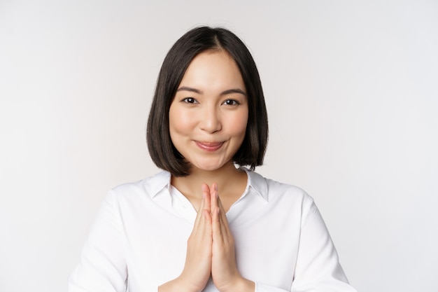 Ciérrese encima del retrato de la mujer japonesa joven que muestra namaste gracias arigatou gesto que se coloca sobre el fondo blanco