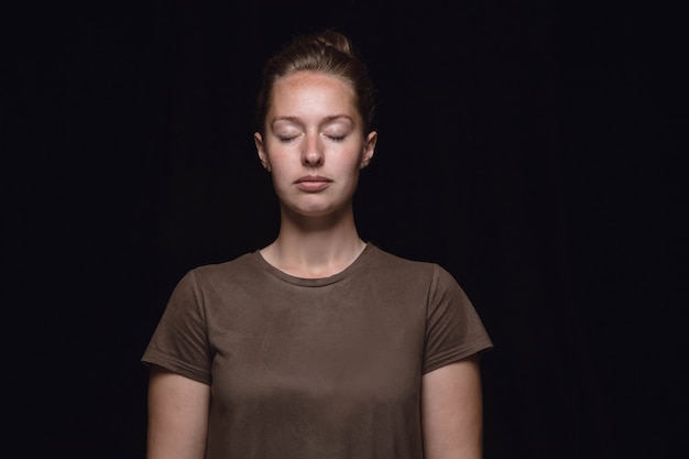 Ciérrese encima del retrato de la mujer joven aislada en el fondo negro del estudio. Photoshot de emociones reales de modelo femenino con los ojos cerrados. Considerado. Concepto de expresión facial, naturaleza humana y emociones.