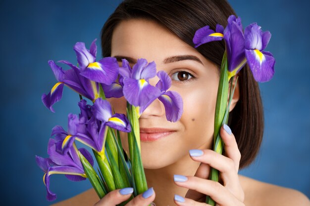 Ciérrese encima del retrato de la mujer joven tierna detrás de las flores violetas sobre la pared azul