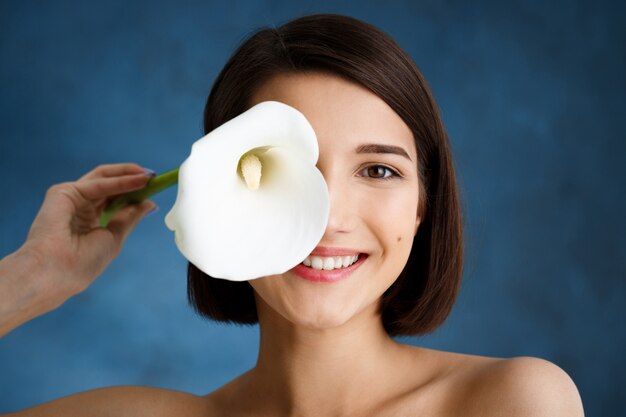 Ciérrese encima del retrato de la mujer joven tierna con la flor blanca sobre la pared azul