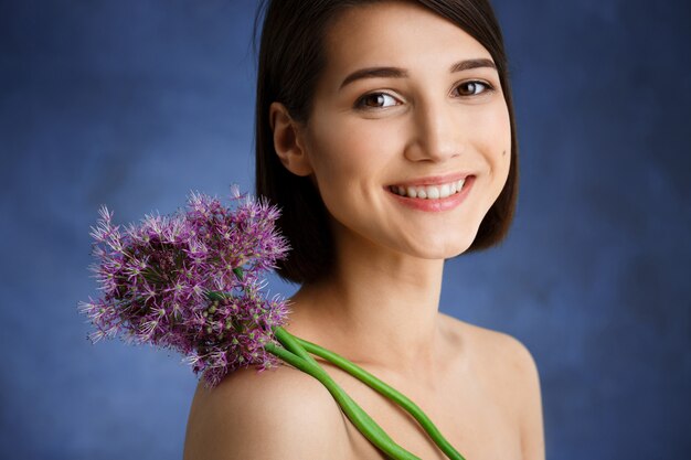 Ciérrese encima del retrato de la mujer joven tierna con la flor de la lila sobre la pared azul