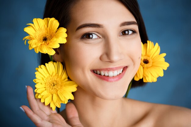 Ciérrese encima del retrato de la mujer joven tierna con las flores amarillas sobre la pared azul