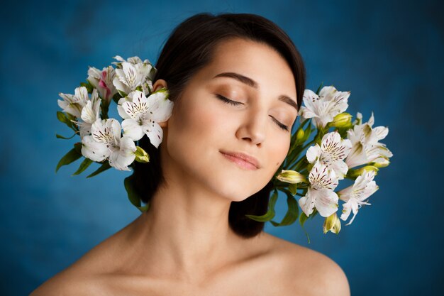 Ciérrese encima del retrato de la mujer joven tierna con las flores blancas sobre la pared azul