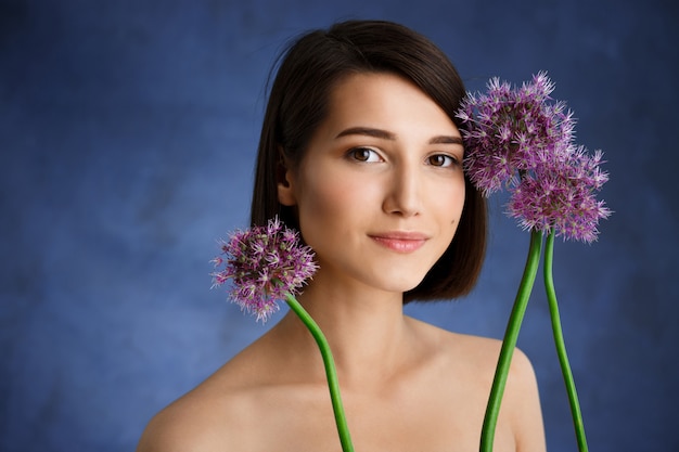 Ciérrese encima del retrato de la mujer joven tierna con las flores de la lila sobre la pared azul