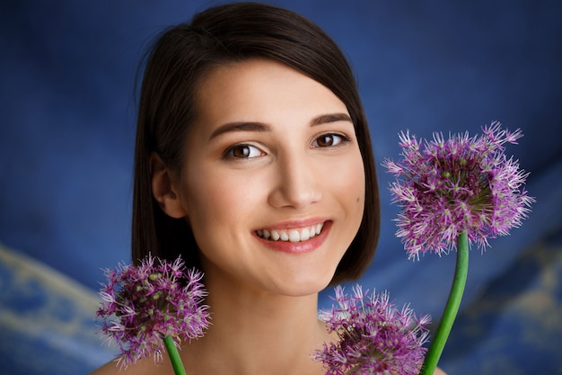 Ciérrese encima del retrato de la mujer joven tierna con las flores de la lila sobre la pared azul