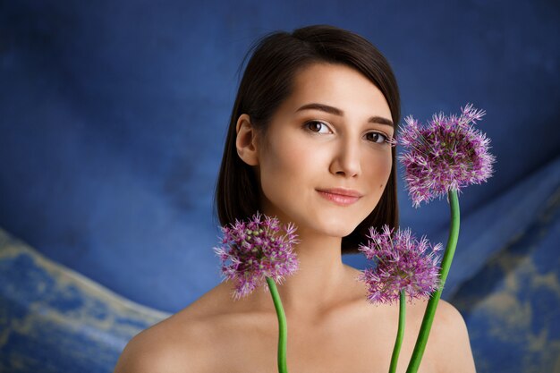 Ciérrese encima del retrato de la mujer joven tierna con las flores de la lila sobre la pared azul