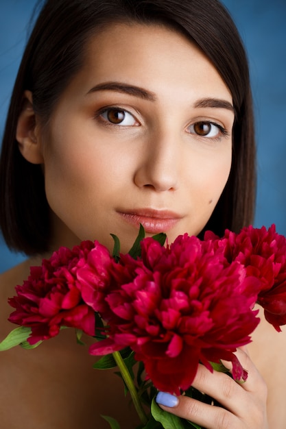 Ciérrese encima del retrato de la mujer joven tierna con las flores rojas sobre la pared azul