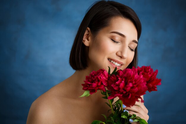 Ciérrese encima del retrato de la mujer joven tierna con las flores rojas sobre la pared azul