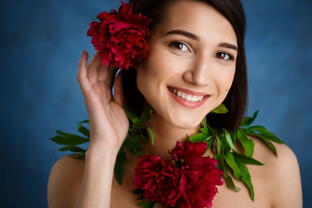 Ciérrese encima del retrato de la mujer joven tierna con las flores rojas sobre la pared azul