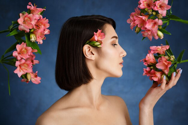 Ciérrese encima del retrato de la mujer joven tierna con las flores rosadas sobre la pared azul