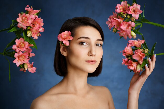 Ciérrese encima del retrato de la mujer joven tierna con las flores rosadas sobre la pared azul