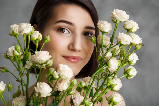 Ciérrese encima del retrato de la mujer joven tierna con las flores sobre la pared gris