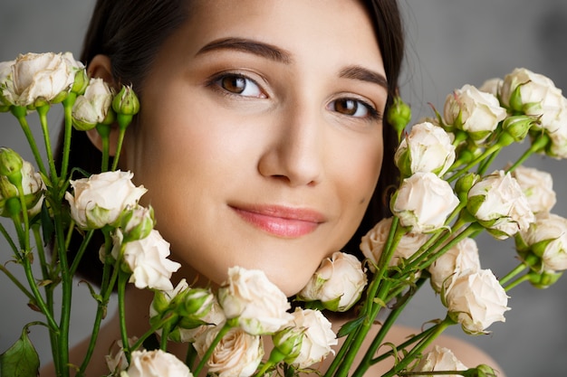 Foto gratuita ciérrese encima del retrato de la mujer joven tierna con las flores sobre la pared gris