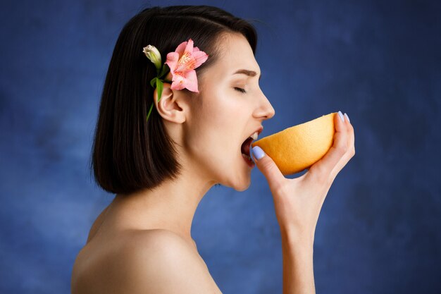 Ciérrese encima del retrato de la mujer joven tierna que sostiene la naranja cortada sobre la pared azul