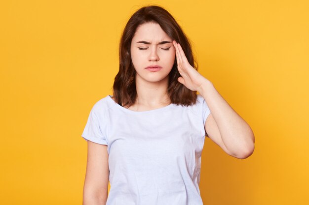 Ciérrese encima del retrato de la mujer morena joven que lleva la camiseta casual blanca aislada sobre amarillo