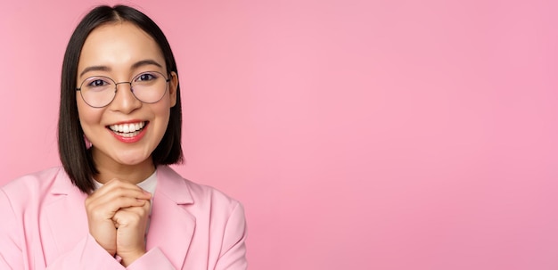 Ciérrese encima del retrato de la mujer de negocios feliz sonriente en los vidrios que aprietan las manos juntas agradecidas emocionadas de rogar algo o decir por favor de pie sobre fondo rosa