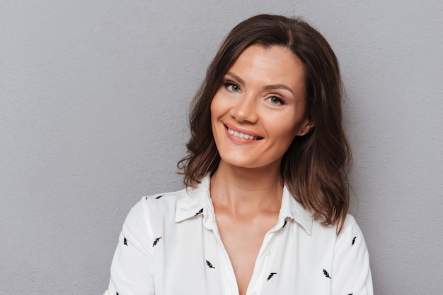 Foto gratuita ciérrese encima del retrato de la mujer sonriente que mira la cámara en gris