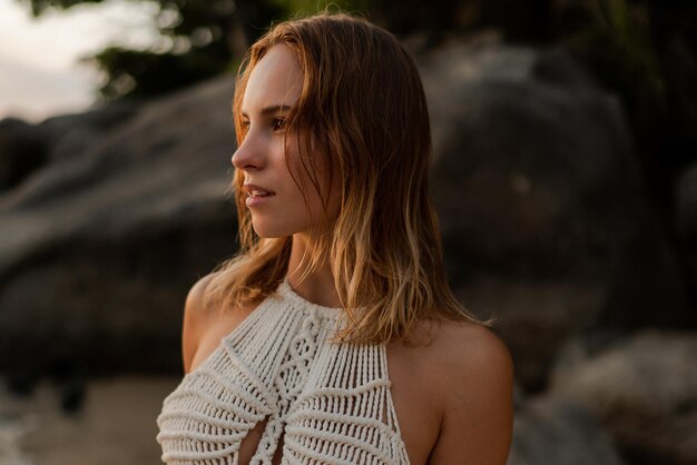 Ciérrese encima del retrato de la mujer en el vestido blanco del ganchillo del boho que presenta en la playa. Foto de moda de verano y vacaciones tropicales.