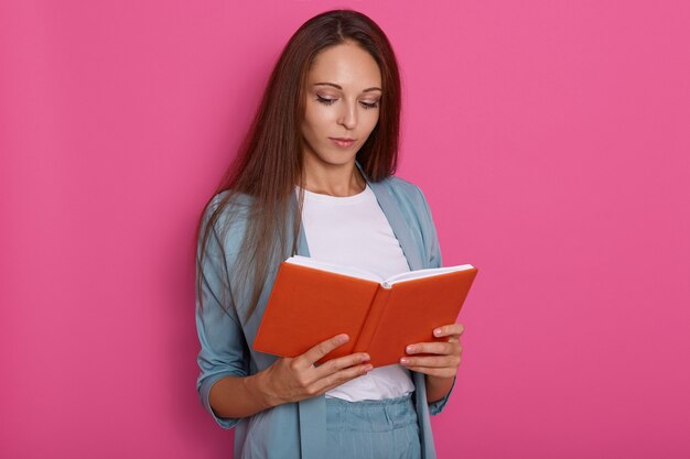 Ciérrese encima del retrato de las mujeres jovenes que leen algo en el cuaderno aislado sobre rosado