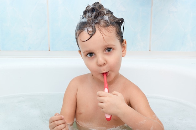 Ciérrese encima del retrato de la niña carming, limpia sus dientes con el cepillo de dientes rojo