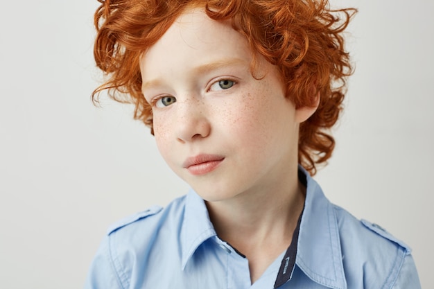 Foto gratuita ciérrese encima del retrato del niño alegre del pelirrojo con las pecas y los ojos grises grandes que miran con la expresión seria.