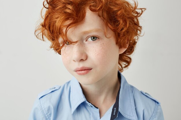 Ciérrese encima del retrato del niño pequeño hermoso con el pelo rizado rojo y los ojos grises que miran con la expresión seria y relajada.