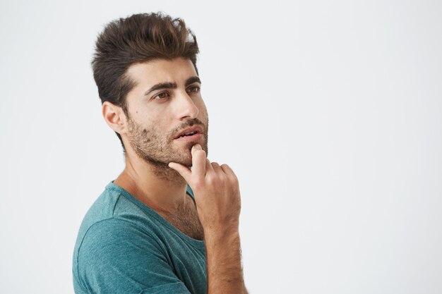 Ciérrese encima del retrato del varón español hermoso en camiseta azul, mirando para arriba con la expresión pensativa, pensando en la cena para hoy. retrato. Expresiones faciales humanas