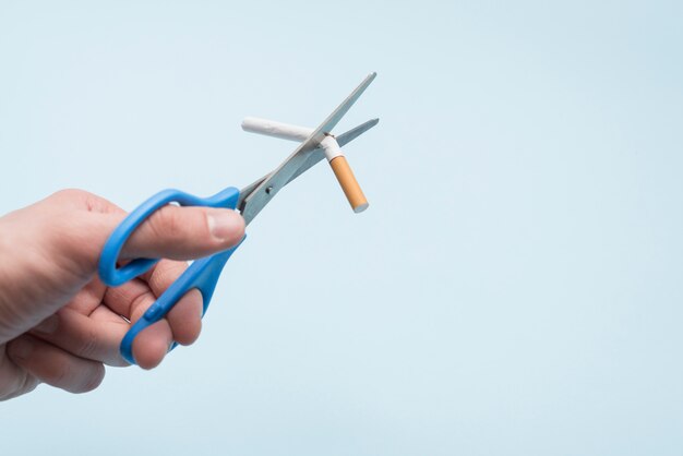 Cigarrillo de Broking de la mano de la persona con tijera sobre fondo azul