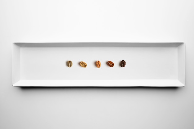 Cinco grados diferentes de tostado de granos de café, aromáticos, desde crudo hasta completamente tostado, aislado en la vista superior de la placa blanca