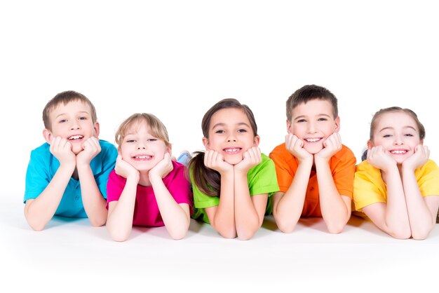 Cinco hermosos niños sonrientes tendidos en el suelo con camisetas de colores brillantes, aislados en blanco.