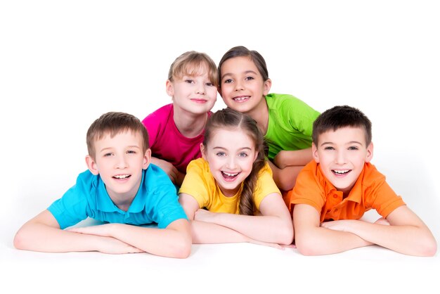 Cinco hermosos niños sonrientes tendidos en el suelo con camisetas de colores brillantes, aislados en blanco.