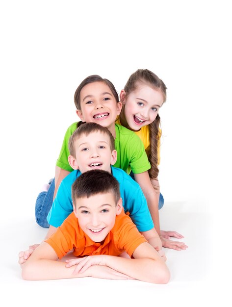 Cinco hermosos niños sonrientes tendidos en el suelo con camisetas de colores brillantes, aislados en blanco.