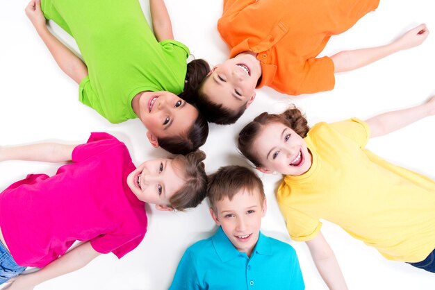 Cinco niños sonrientes tirados en el suelo en círculo con camisetas brillantes. Vista superior. Aislado en blanco.
