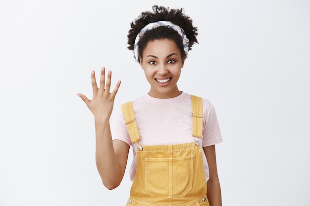 Cinco razones para decir que sí. Retrato de una joven afroamericana feliz y relajada de buen aspecto con un mono amarillo y una diadema de moda que muestra la palma o el quinto lugar que tomó en la competencia