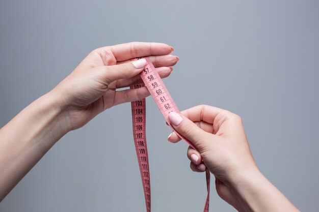 La cinta en manos femeninas en gris. Concepto de pérdida de peso, dieta y desintoxicación