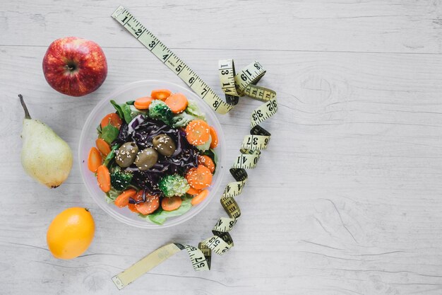 Cinta métrica cerca de ensalada y frutas