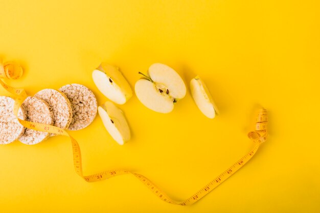 Cinta métrica cerca de rebanadas de fruta y pan crujiente