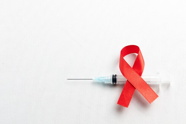 Cinta roja y jeringa con fondo blanco. Cinta de concienciación sobre el VIH / SIDA