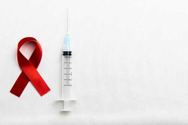 Cinta roja y jeringa con fondo blanco. Cinta de concienciación sobre el VIH / SIDA