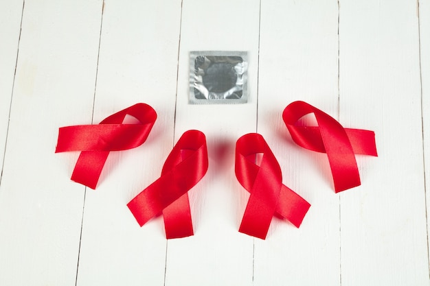 Cinta roja de la muestra de la conciencia del sida en el fondo blanco de la tabla de madera con el condón. Concepto del Día Mundial del Sida. La salud, la ayuda, la atención, el apoyo, la esperanza, la enfermedad, el concepto de salud