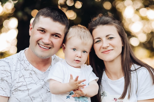 Cintura para arriba de la madre sonriente y el padre abrazando a su pequeño hijo mientras se quedan juntos al aire libre