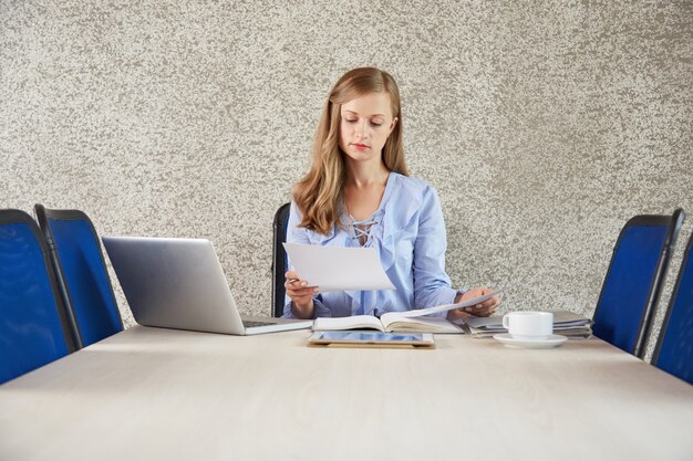Cintura de mujer de negocios joven sentada en el escritorio en la oficina mirando el documento