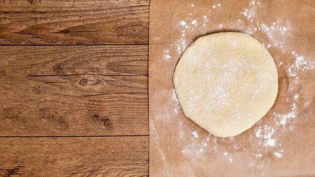 La circular cruda aplana la masa en papel pergamino sobre la mesa de madera