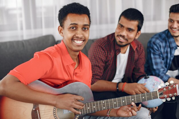 Círculo de amigos diversos reunidos en casa. Un chico cantando mientras toca la guitarra.