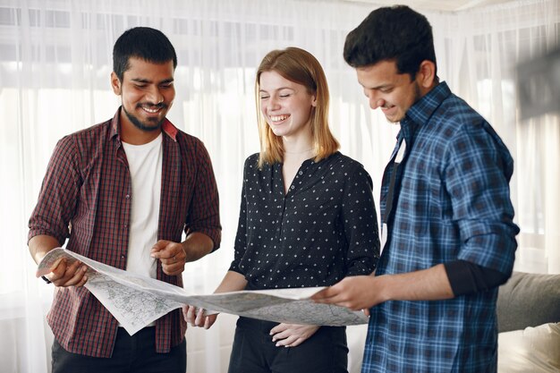 Círculo feliz de amigos planeando un viaje. Trotamundos inspeccionando un mapa estando en casa. Etnia europea e india.