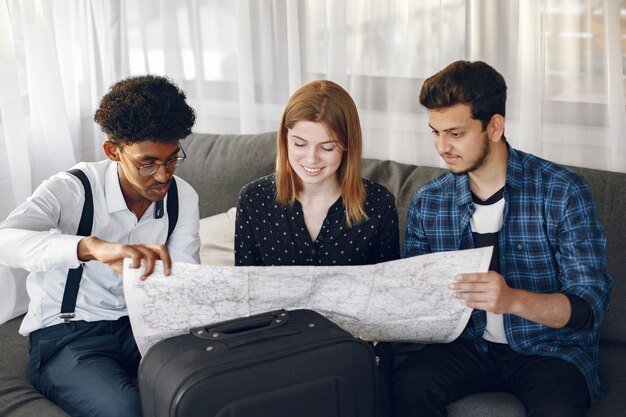 Círculo feliz de amigos planeando un viaje. Trotamundos inspeccionando un mapa estando en casa. Etnia europea e india.