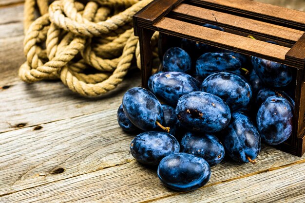 Ciruelas azules en un cajón de madera en una composición rústica