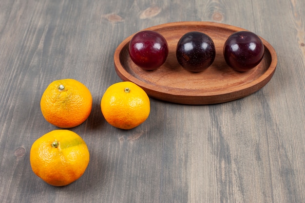 Ciruelas deliciosas con deliciosas mandarinas en una mesa de madera. Foto de alta calidad