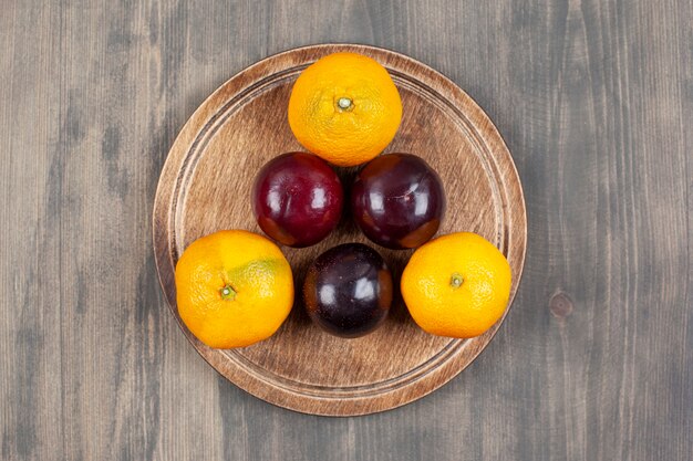 Ciruelas deliciosas con deliciosas mandarinas en una placa de madera. Foto de alta calidad